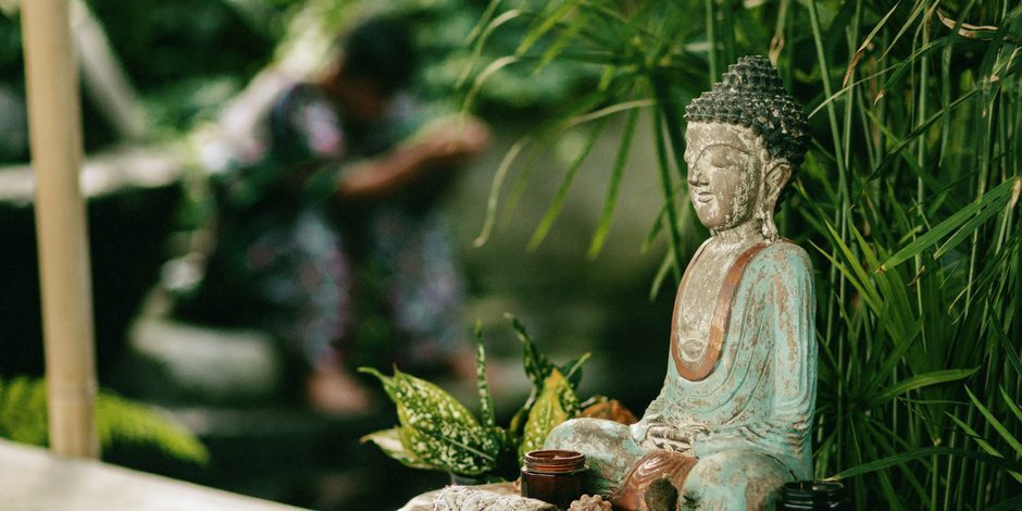 a weathered Buddha statue among ferns in the Bali jungle